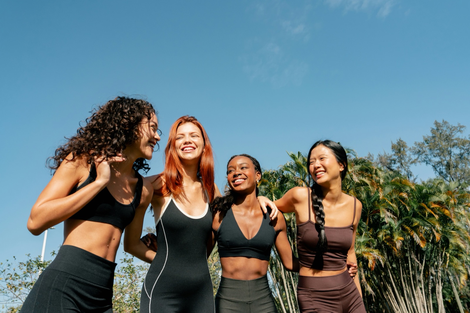 Four diverse friends laughing together under a clear sky.